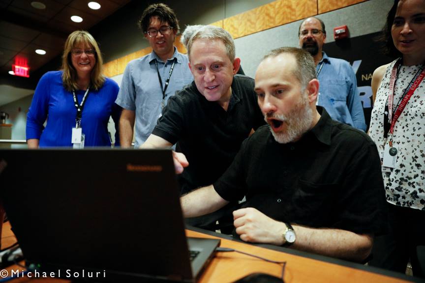 Alan Stern (center) and members of the New Horizons science team react to seeing new images of Pluto for the first time. Credit: Michael Soluri